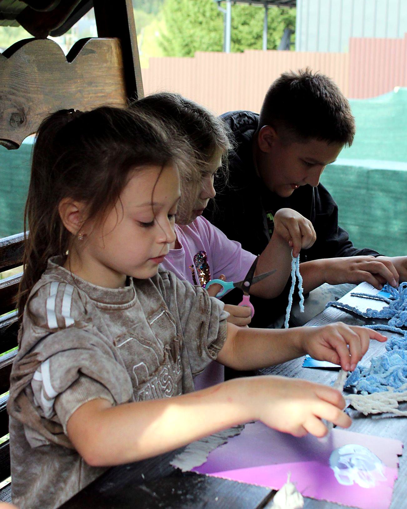 Children working on a yarn-and-paper art project at an outdoor table
